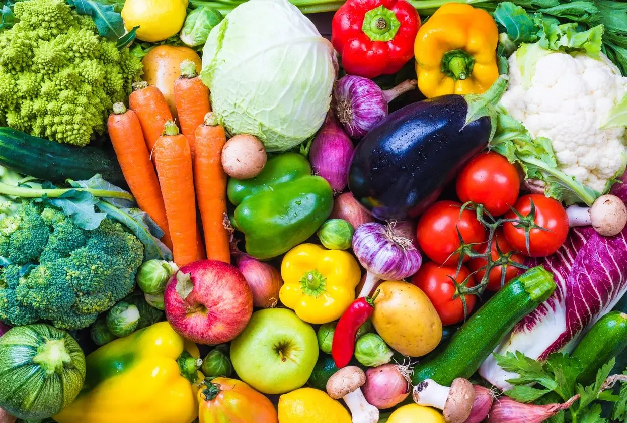 A pile of fruits and vegetables including tomatoes, apples, carrots, cucumbers, radishes, peppers, onions, garlic, cabbage, broccoli ,